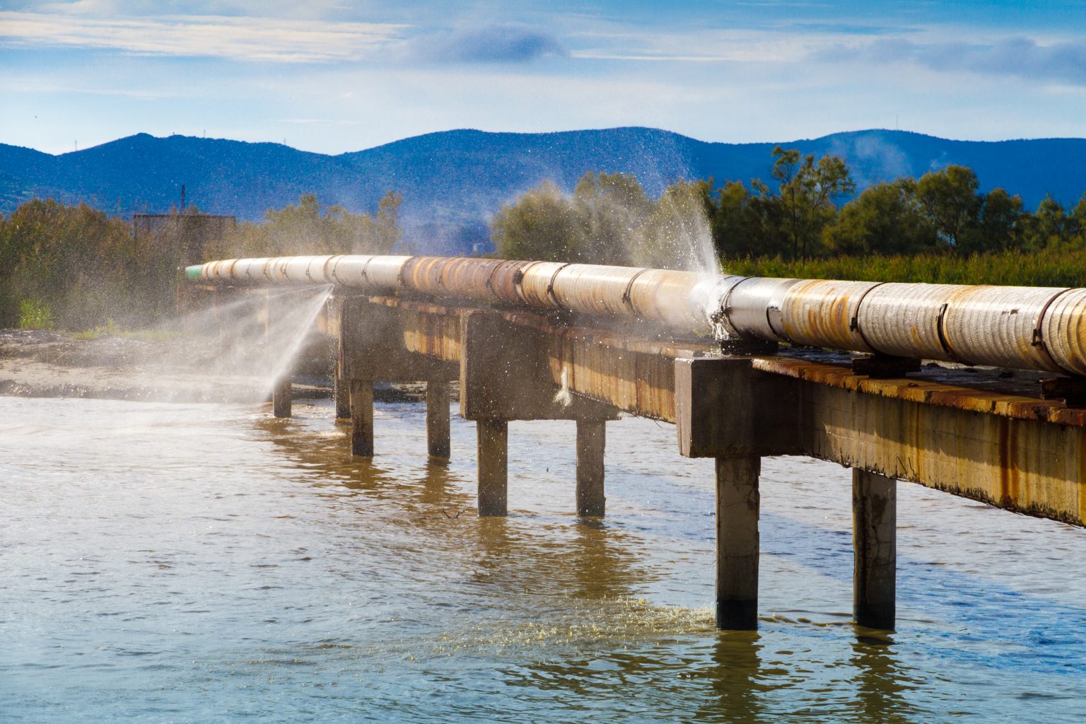 A pipe that crosses a waterbody is also spraying water.