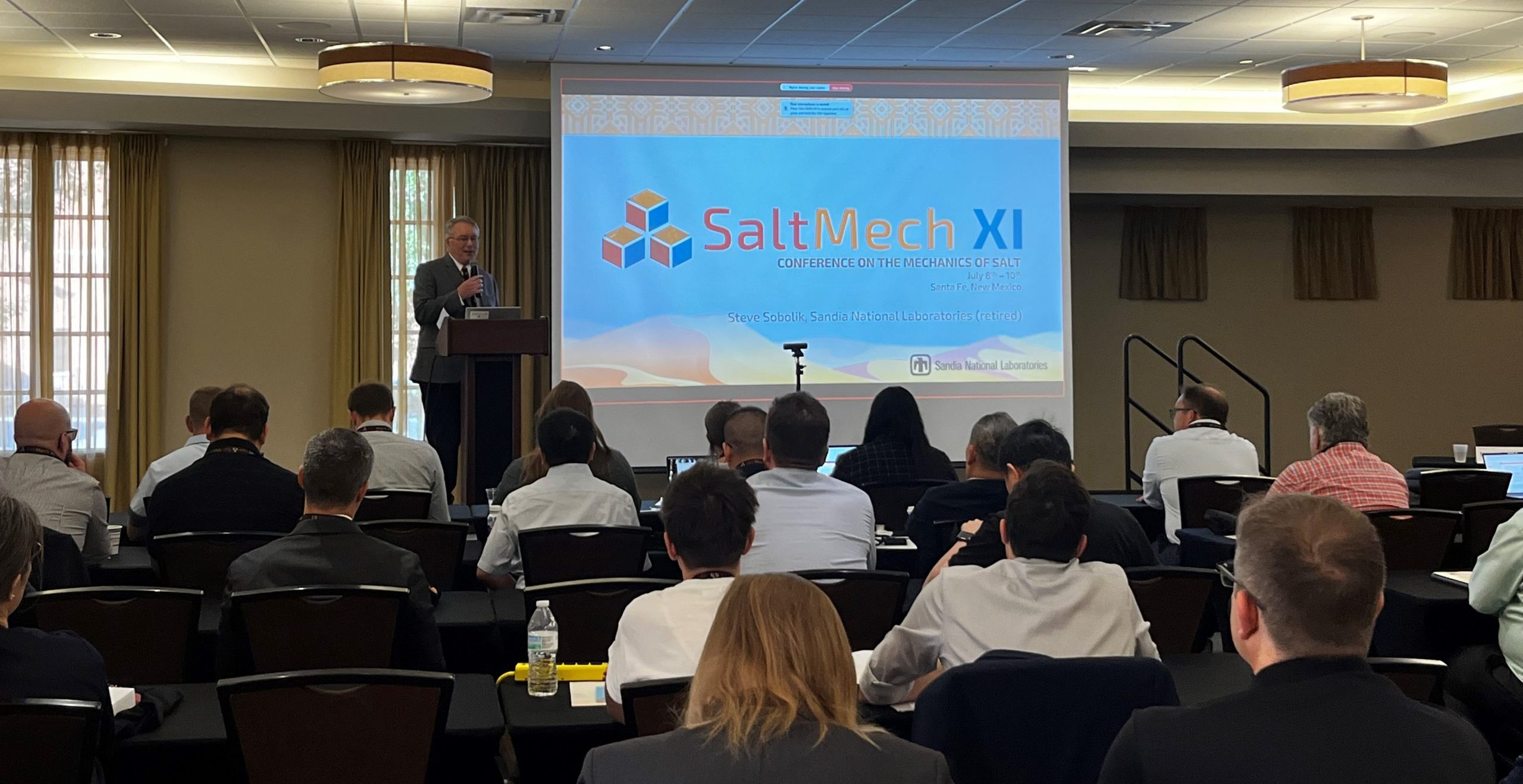 A man stands in front of a crowd in a conference room giving a presentation