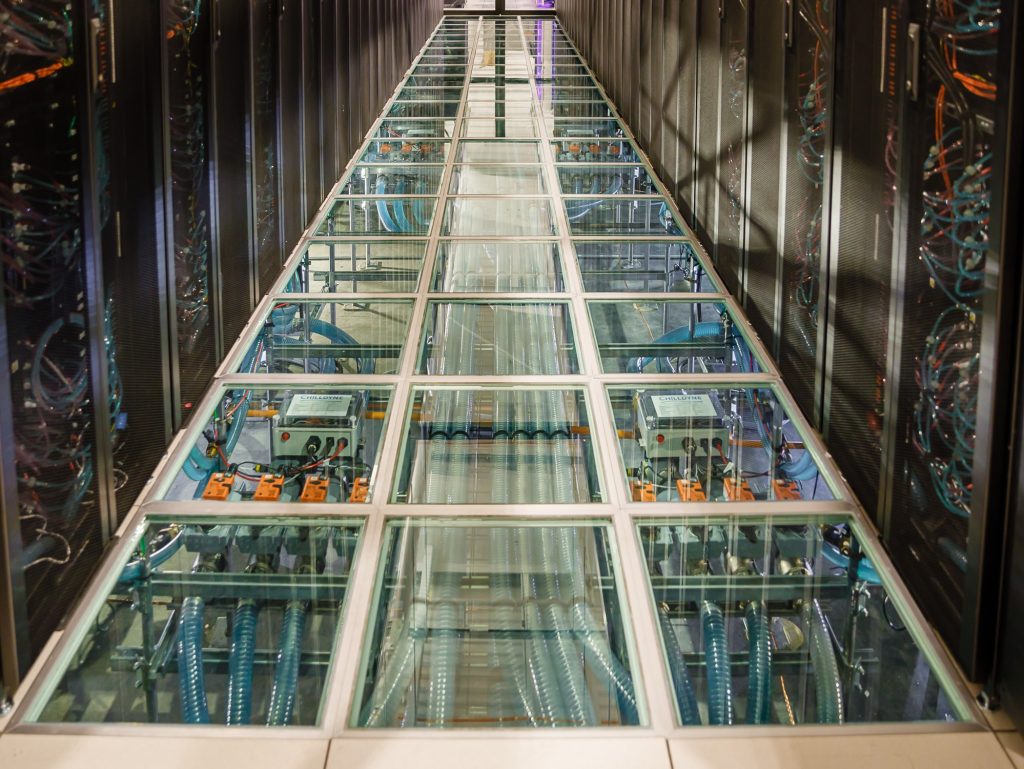 Computers surround a transparent floor that shows wires and electronic equipment below it.