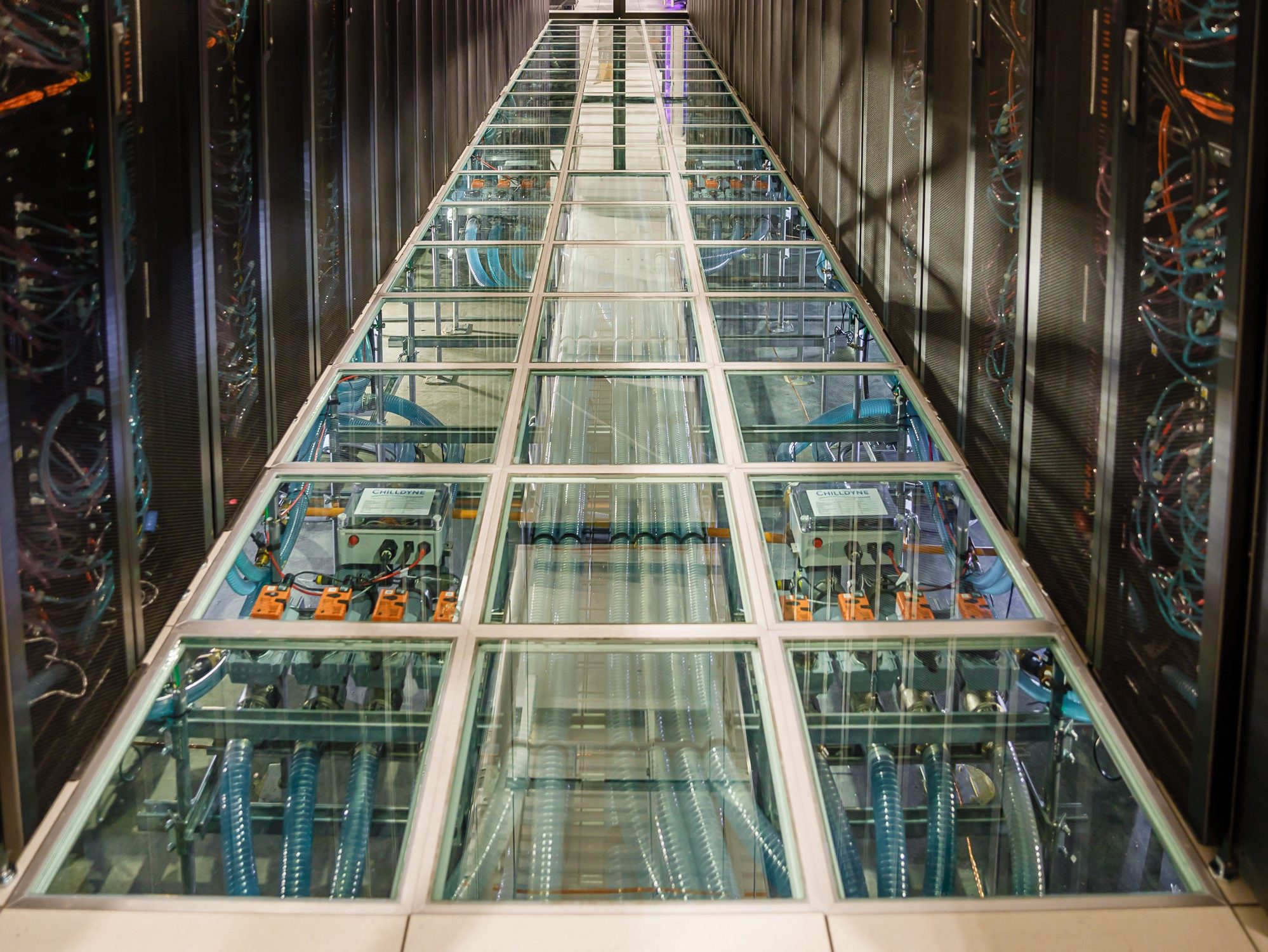 Computers surround a transparent floor that shows wires and electronic equipment below it.