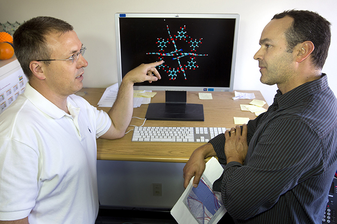 Vitalie Stavila, left, and Catalin Spataru discuss modeling approaches to conduct electronic structure calculations. The TCNQ molecule changes the MOF’s properties to enable thermoelectric conductivity. (Photo by Dino Vournas)