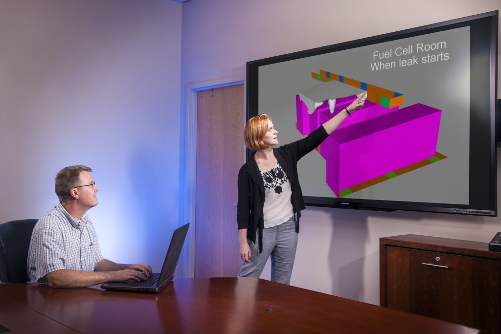 photo of two scientists. One is standing and pointing to a fuel cell graphic while the other watches