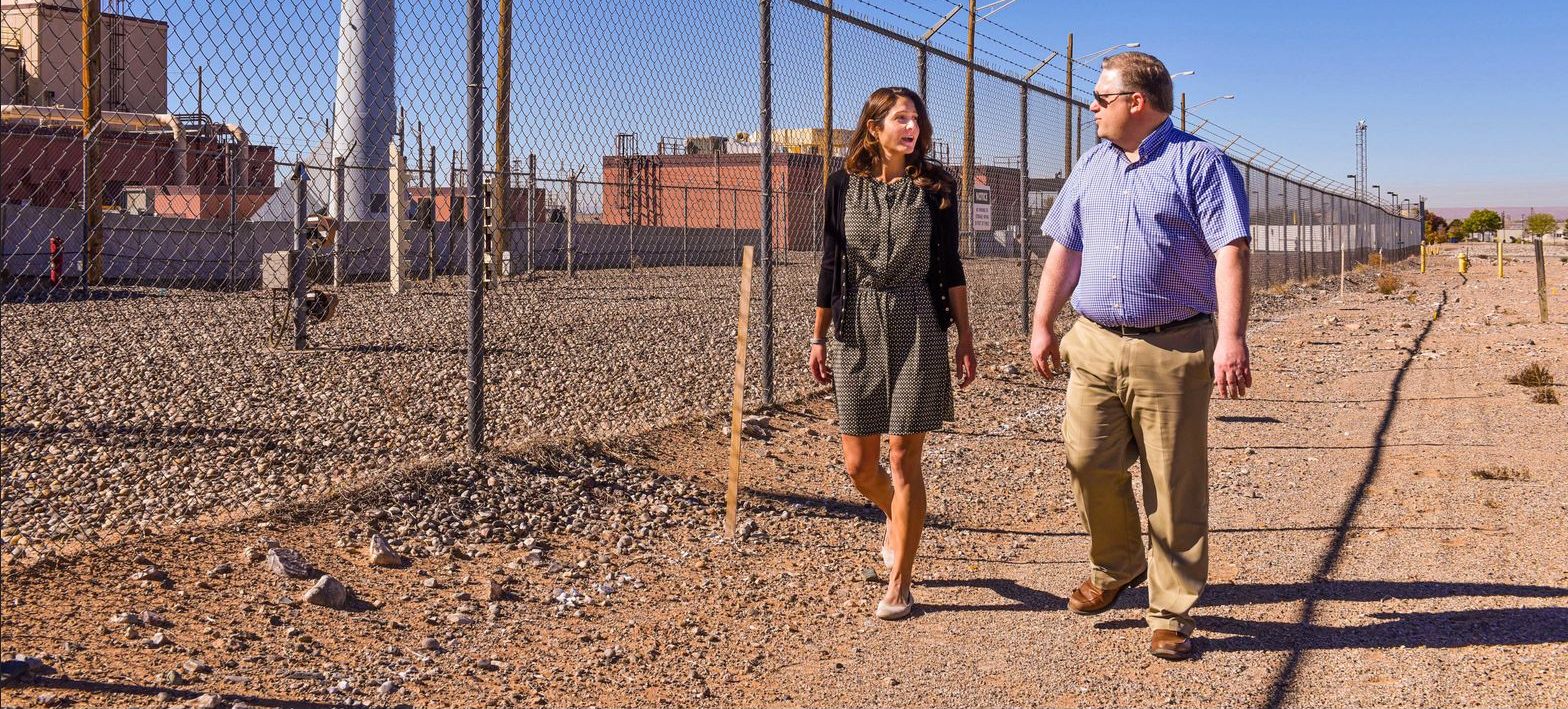 two Sandia National Laboratories nuclear engineers, stroll outside of a nuclear facility. Recently they updated a consequence assessment code so that it can model the health and economic impacts of an unlikely accident practically to a facility’s fence. (Photo by Randy Montoya)