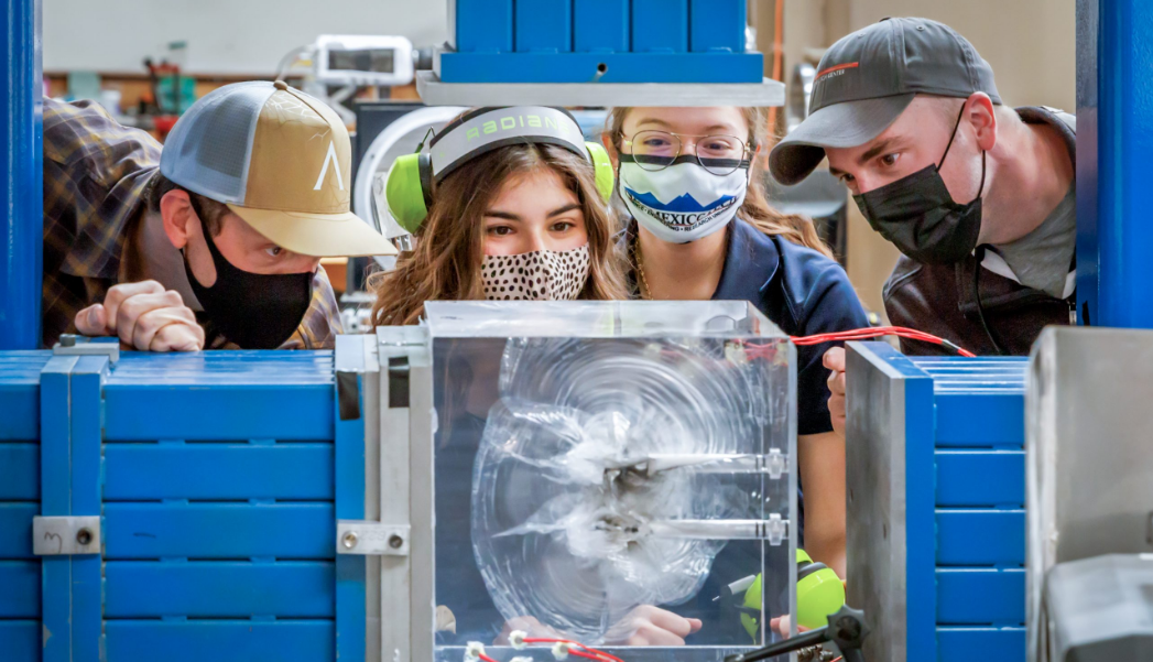 Technicians and students examine a plexiglass cube fractured by a small explosion
