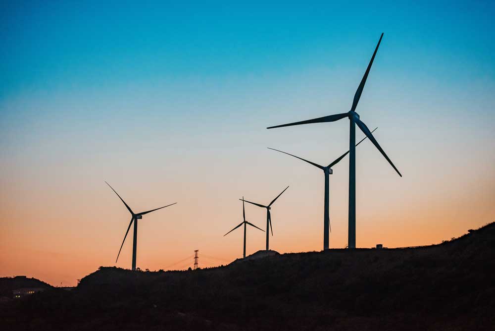 wind turbines spin on the horizon silhouetted by a sunset
