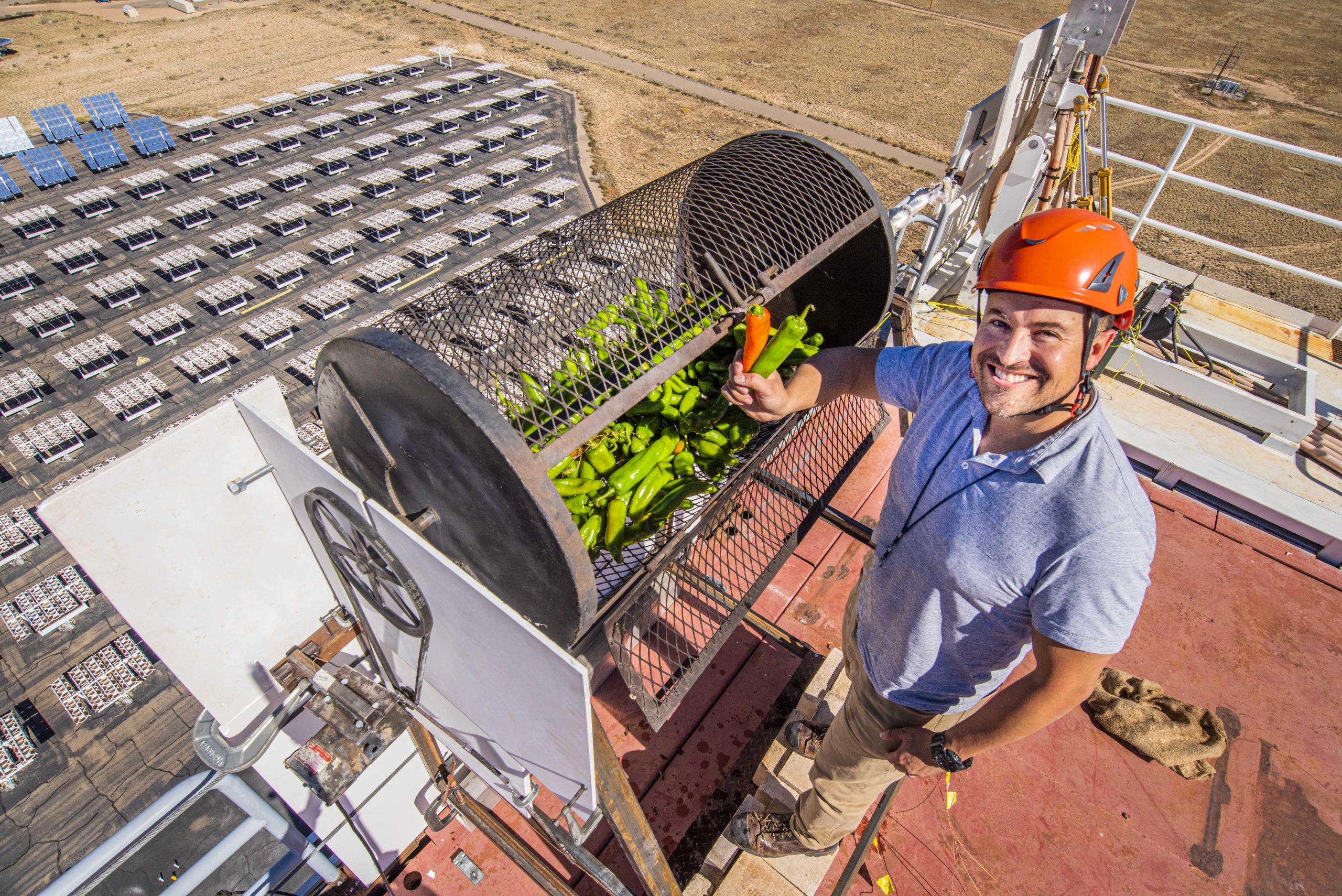 An engineer stands atop the national solar thermal test facility's tower and holds green chiles aloft