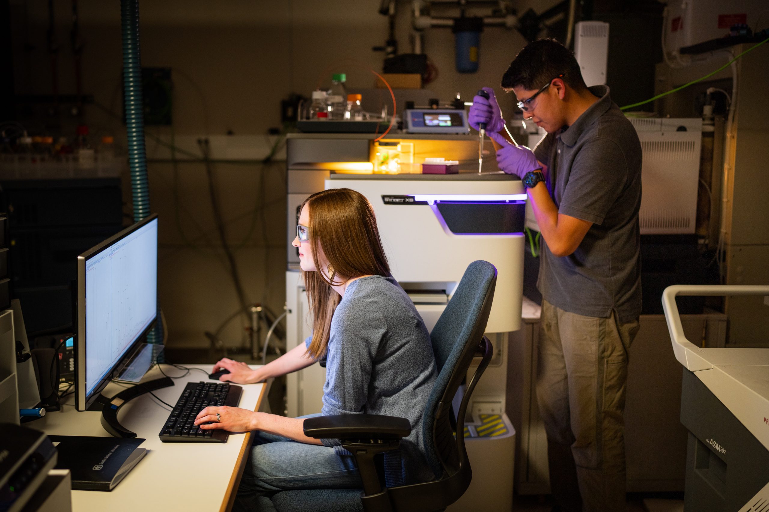 Jessica Kustas, left, and Andre Benally work with a mass spectrometer at Sandia National Laboratories while trying to pair up technologies to go beyond just absorbing PFAS. (Photo by Craig Fritz)