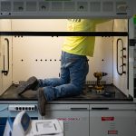 A person kneels while working inside a lab hood