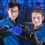 Two researchers hold up a scintillator, a blue disk