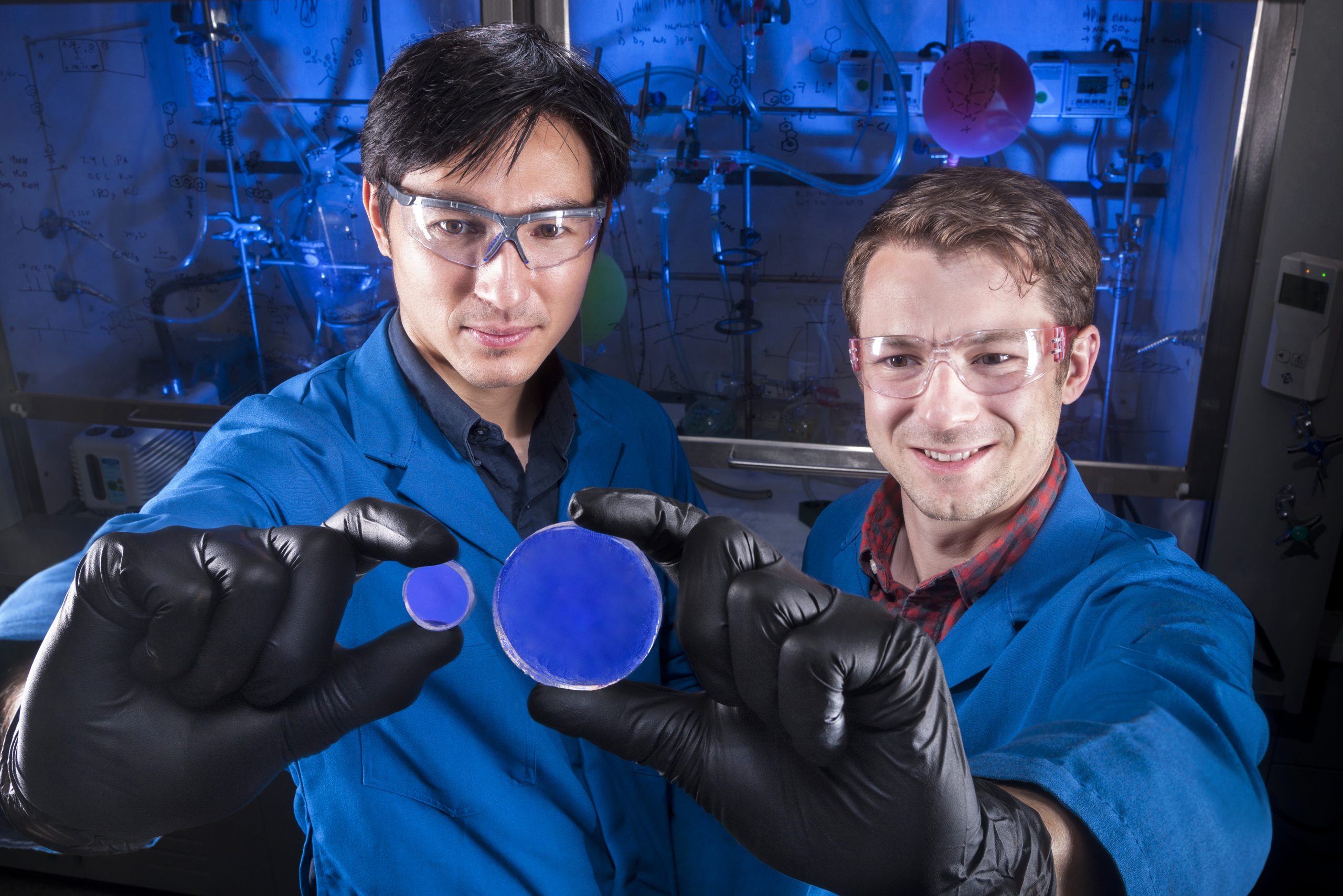 Two researchers hold up a scintillator, a blue disk