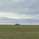 A verdant arctic tundra extends to the horizon. A small hill is apparent in the middle of the tundra -- it is a A permafrost-created pingo or “ice pimple” in the North Slope of Alaska.